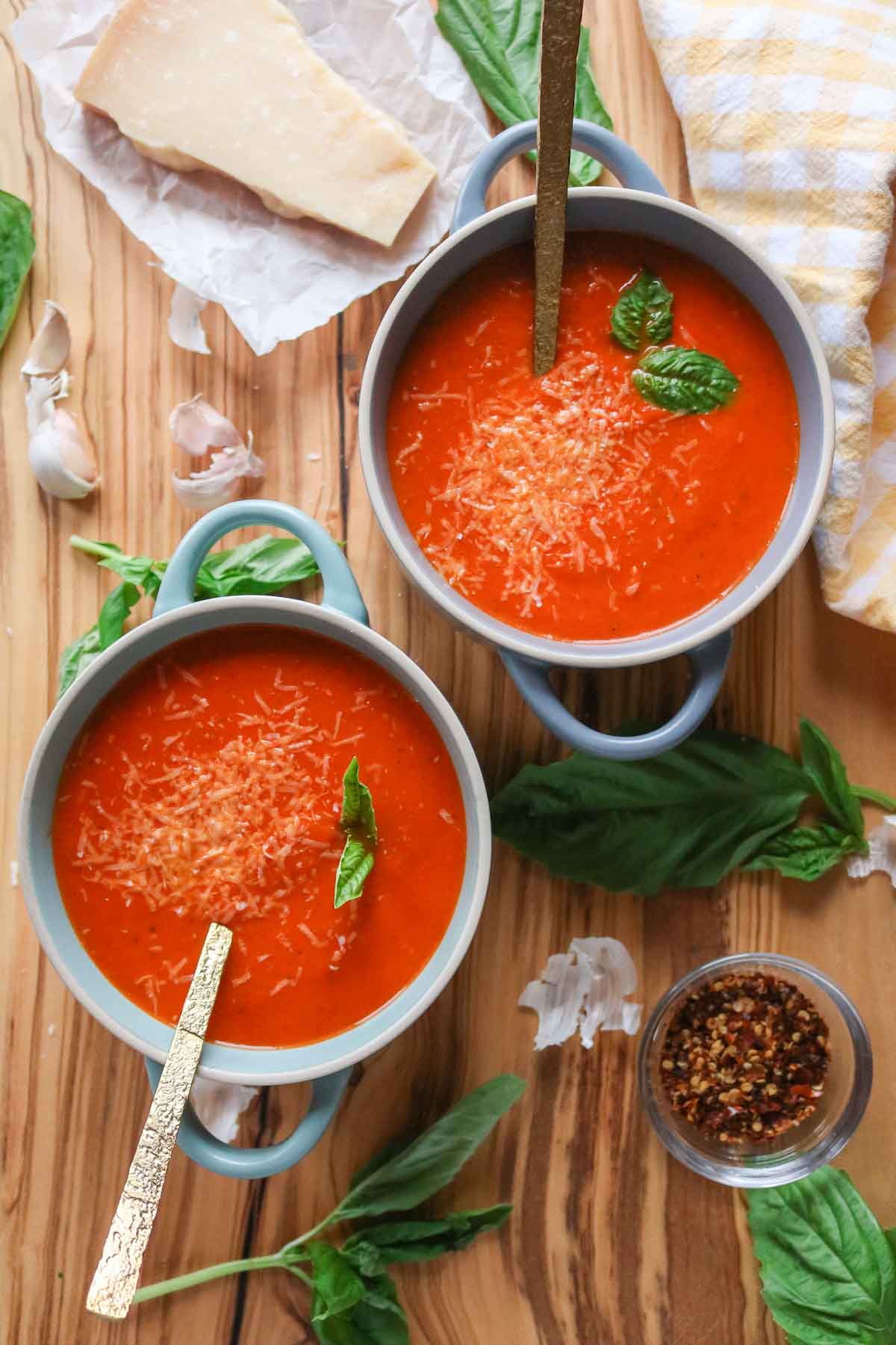 Two bowls of creamy tomato basil soup garnished with cheese and basil.