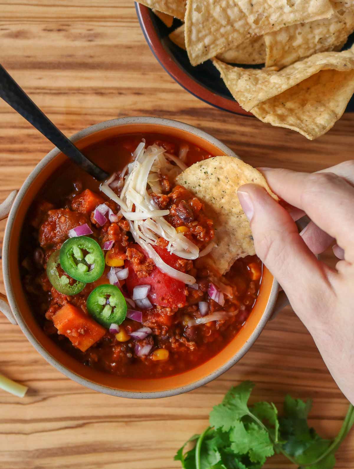 Hand holding a tortilla chip, dipping it into a bowl of chili.