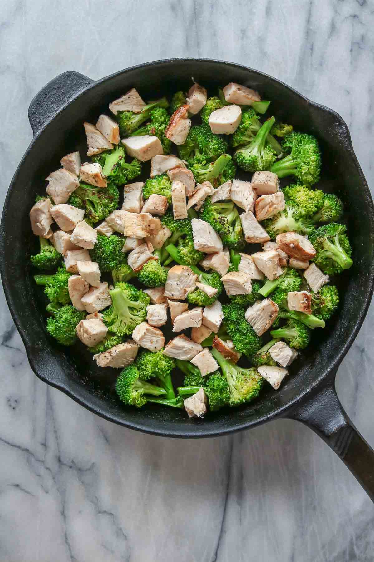 Cubes of cooked chicken and broccoli florets in a skillet.