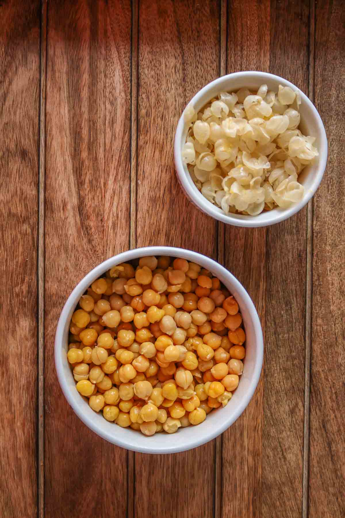Bowl of peeled chickpeas next to a bowl of the chickpea skins.