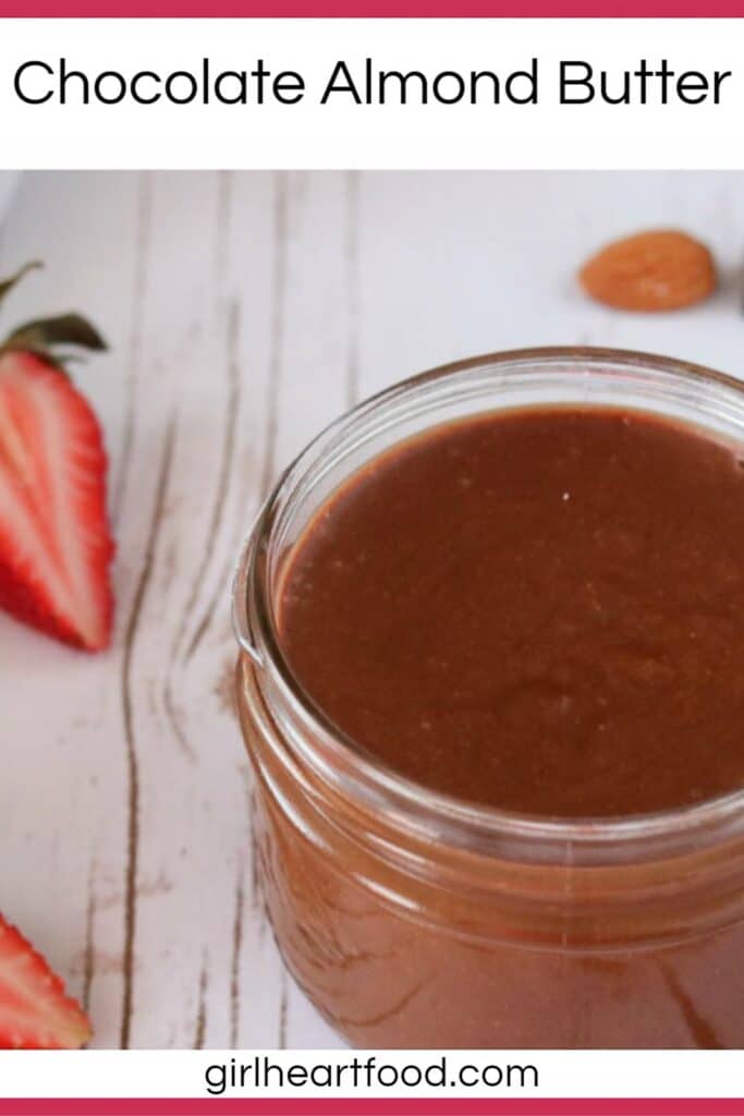 Jar of chocolate almond butter next to a cut strawberry and an almond.