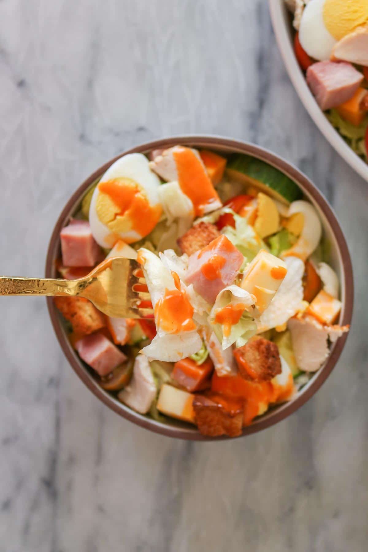 Forkful of chef salad from a bowl.