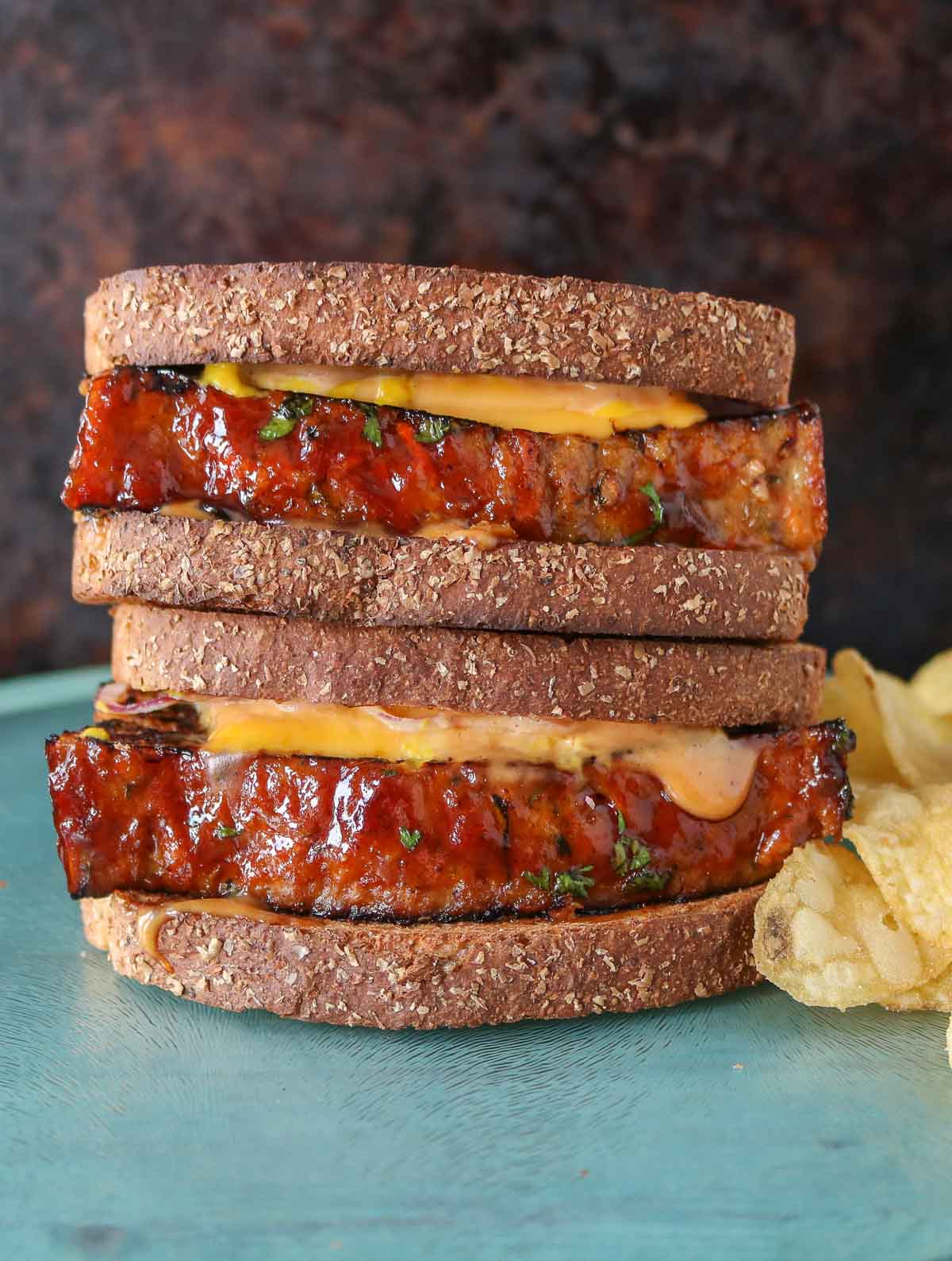 Stack of two meatloaf sandwiches next to potato chips.