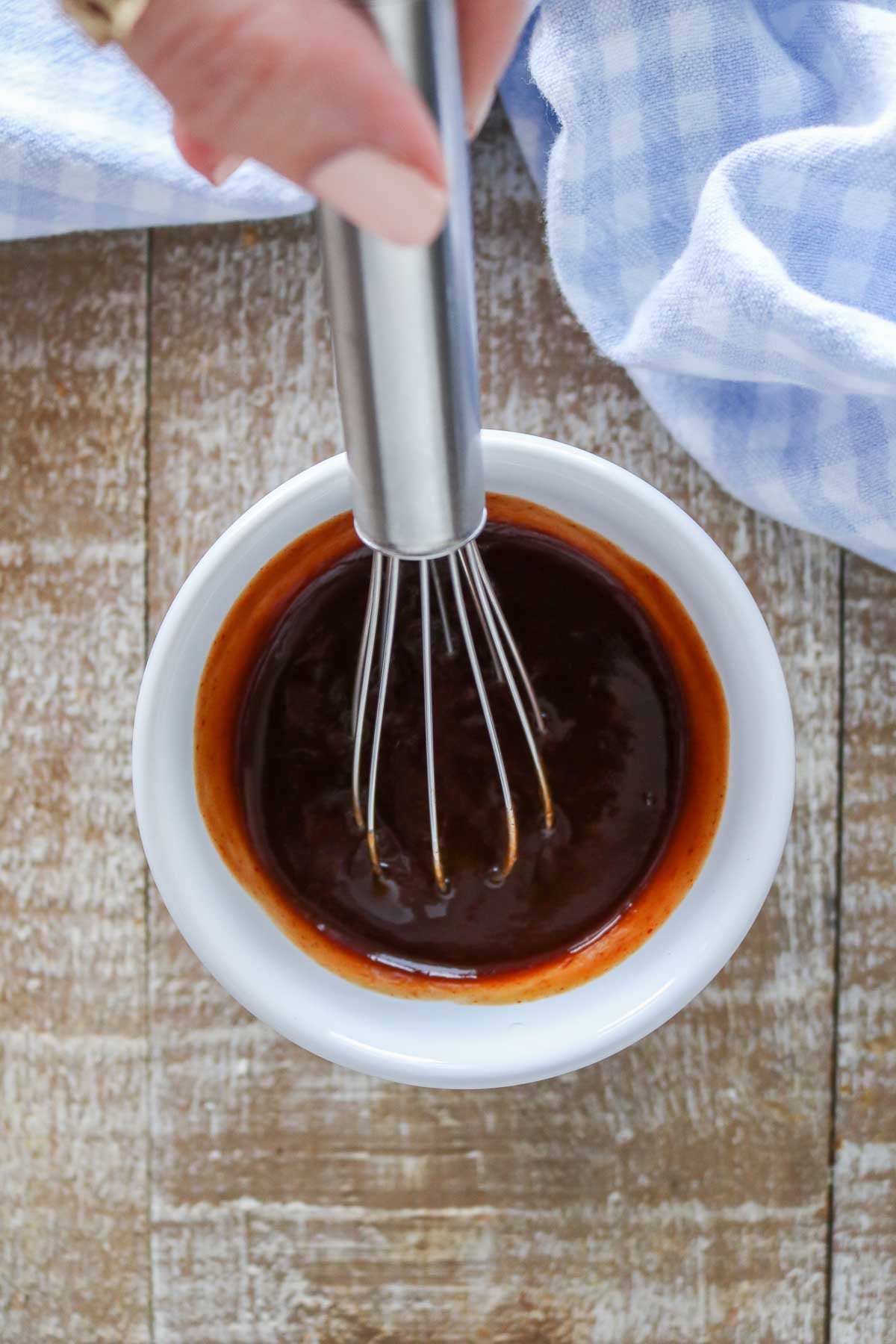 Hand holding a whisk, mixing up sauce for meatloaf in a bowl.