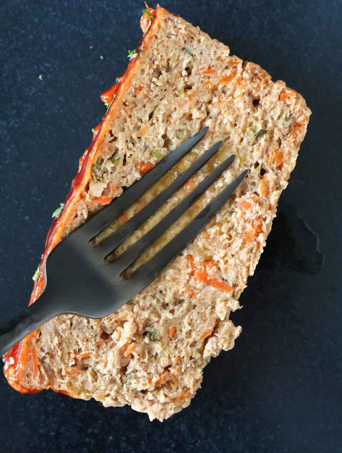 Fork pressing down on a slice of meatloaf, showing how juicy it is.