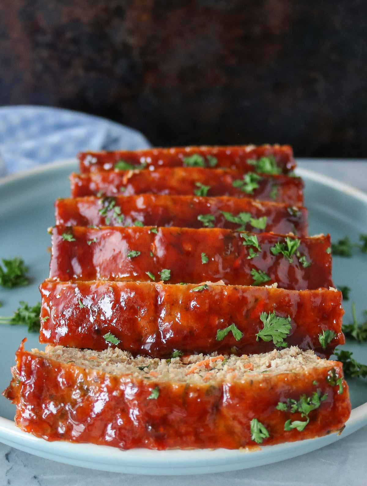Sliced ground chicken meatloaf on a plate, showing the sauce-covered top.