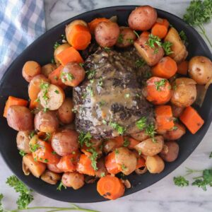 Moose roast and vegetables topped with parsley and gravy on a serving platter.