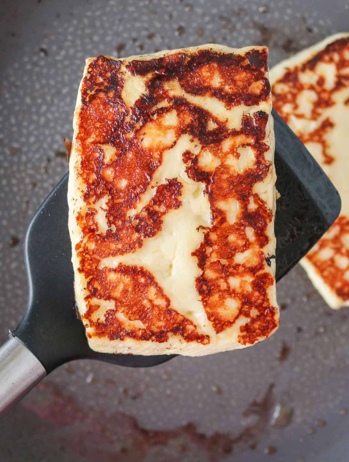 Spatula scooping up a portion of pan-fried halloumi cheese from a pan.