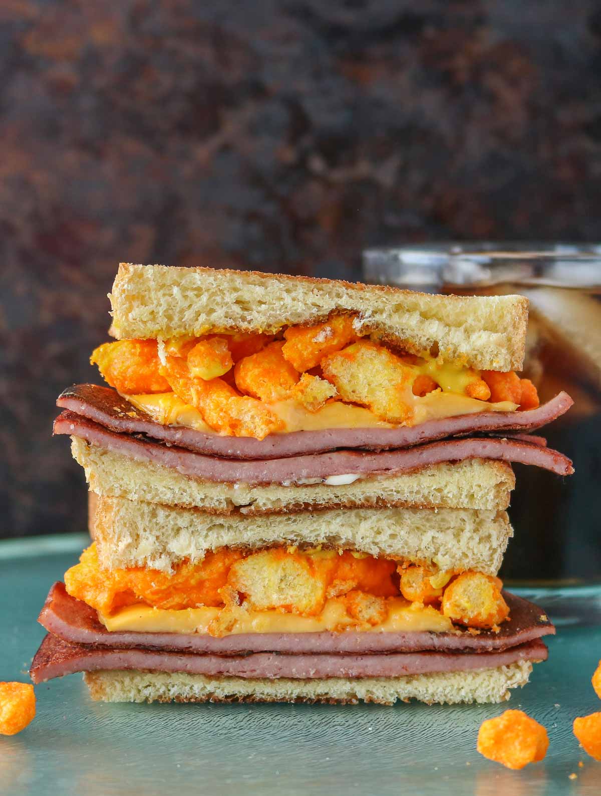 Stack of two halves of a fried bologna sandwich in front of a glass of soda.