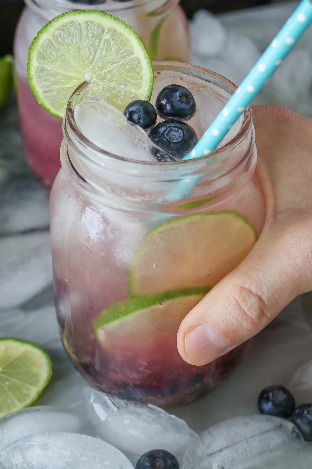 Hand holding a glass jar of lime blueberry mocktail.