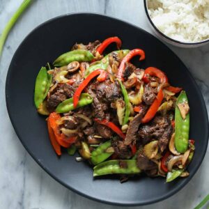 Moose stir-fry on a serving platter next to a bowl of rice.