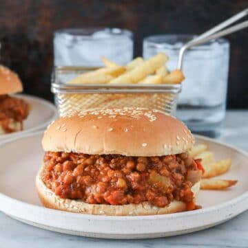 Vegan sloppy joe and a basket of French fries on a plate in front of two glasses of water.