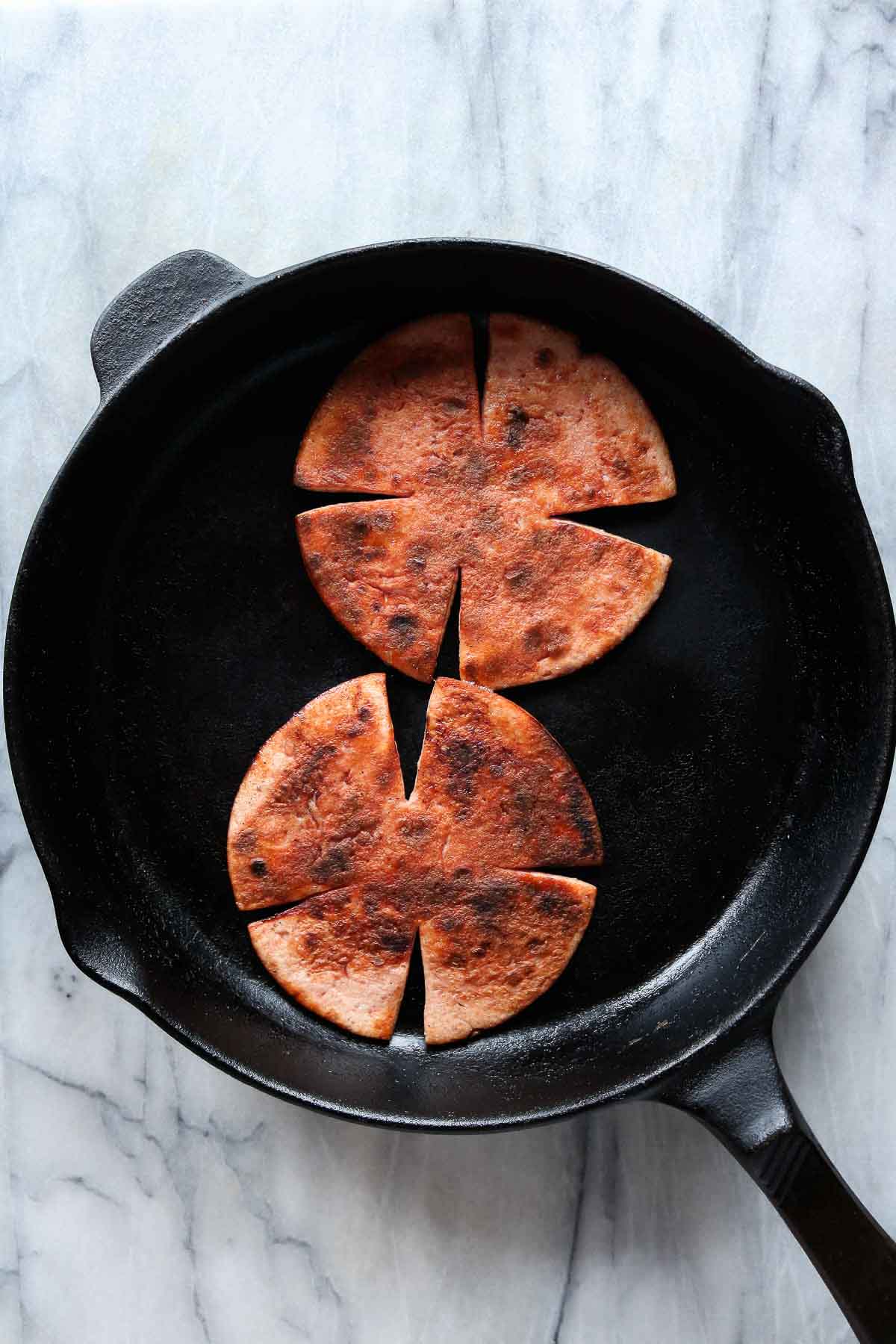 Two slices of bologna frying in a cast-iron skillet.