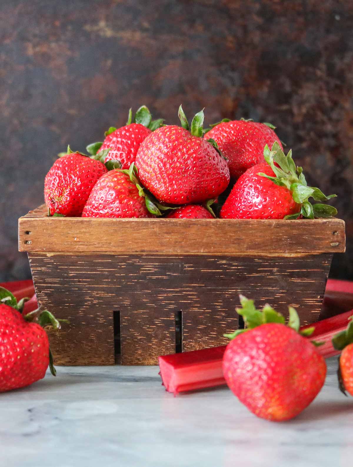 Basket of strawberries alongside stalks of rhubarb.