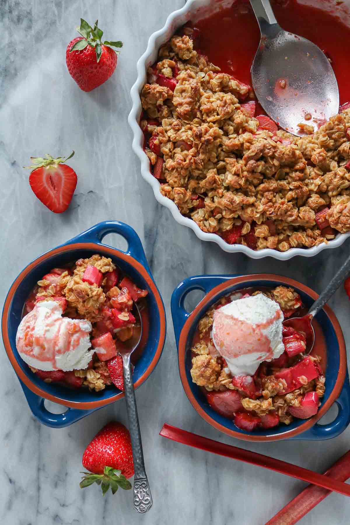 Two portions of fruit crisp with ice cream alongside a serving dish of the fruit crisp.