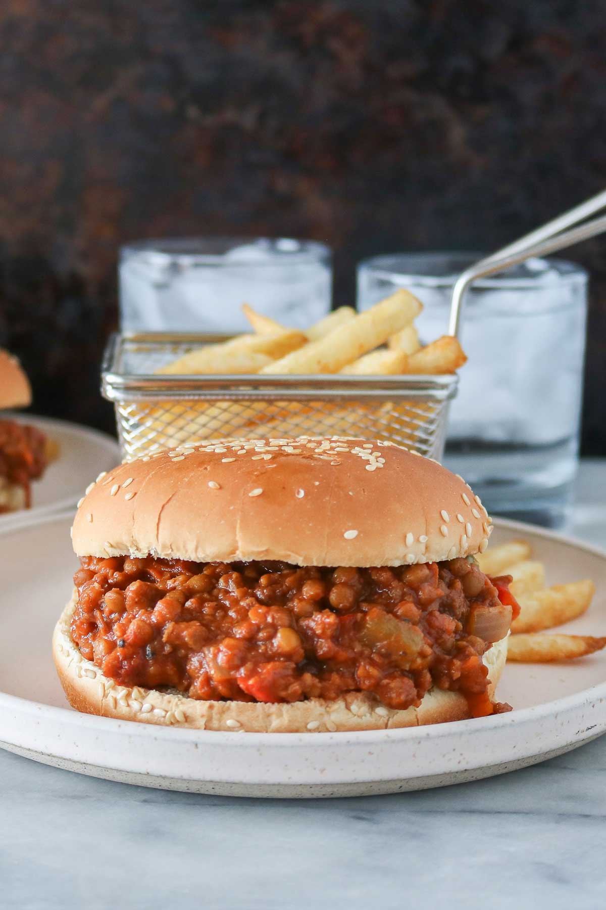 Vegan sloppy joe and basket of fries on a plate in front of two glasses of water.