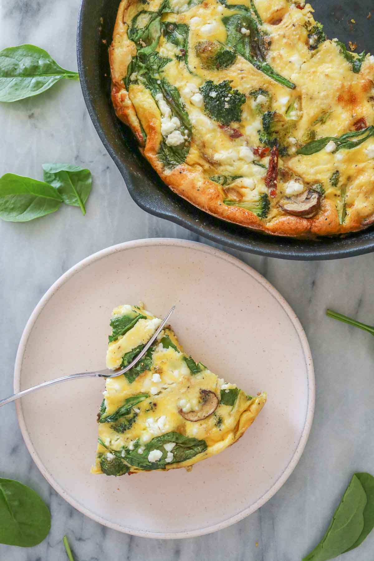 Slice of vegetable frittata on a plate next to a skillet of the frittata.