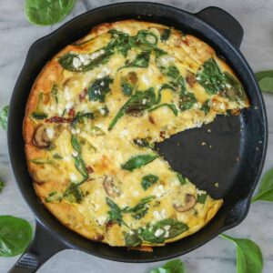 Vegetable frittata in a skillet with a piece removed.