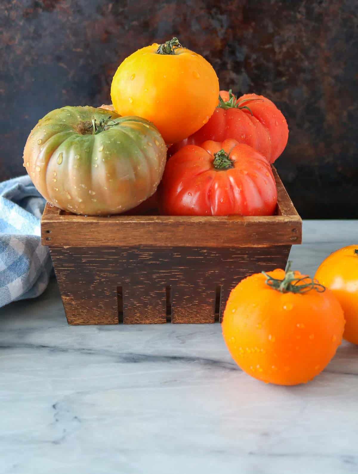 Heirloom tomatoes, some in a brown wooden carton and some on a marble board.