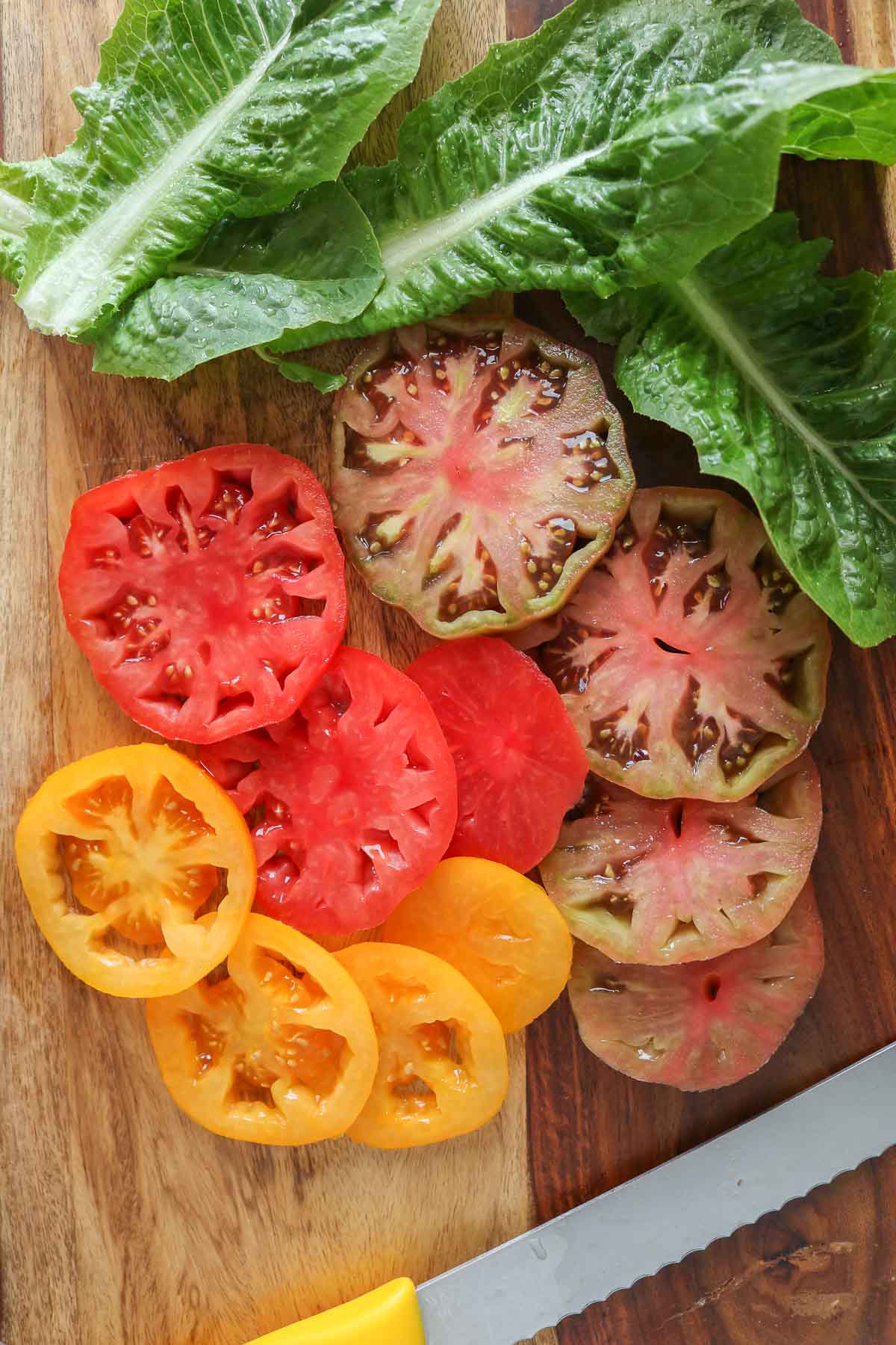 Sliced heirloom tomatoes and leaves of lettuce on a cutting board with a knife.