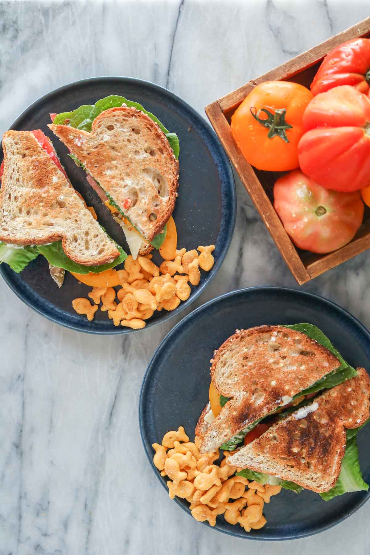 Overhead shot of two toasted tomato sandwiches, each on a plate with crackers.