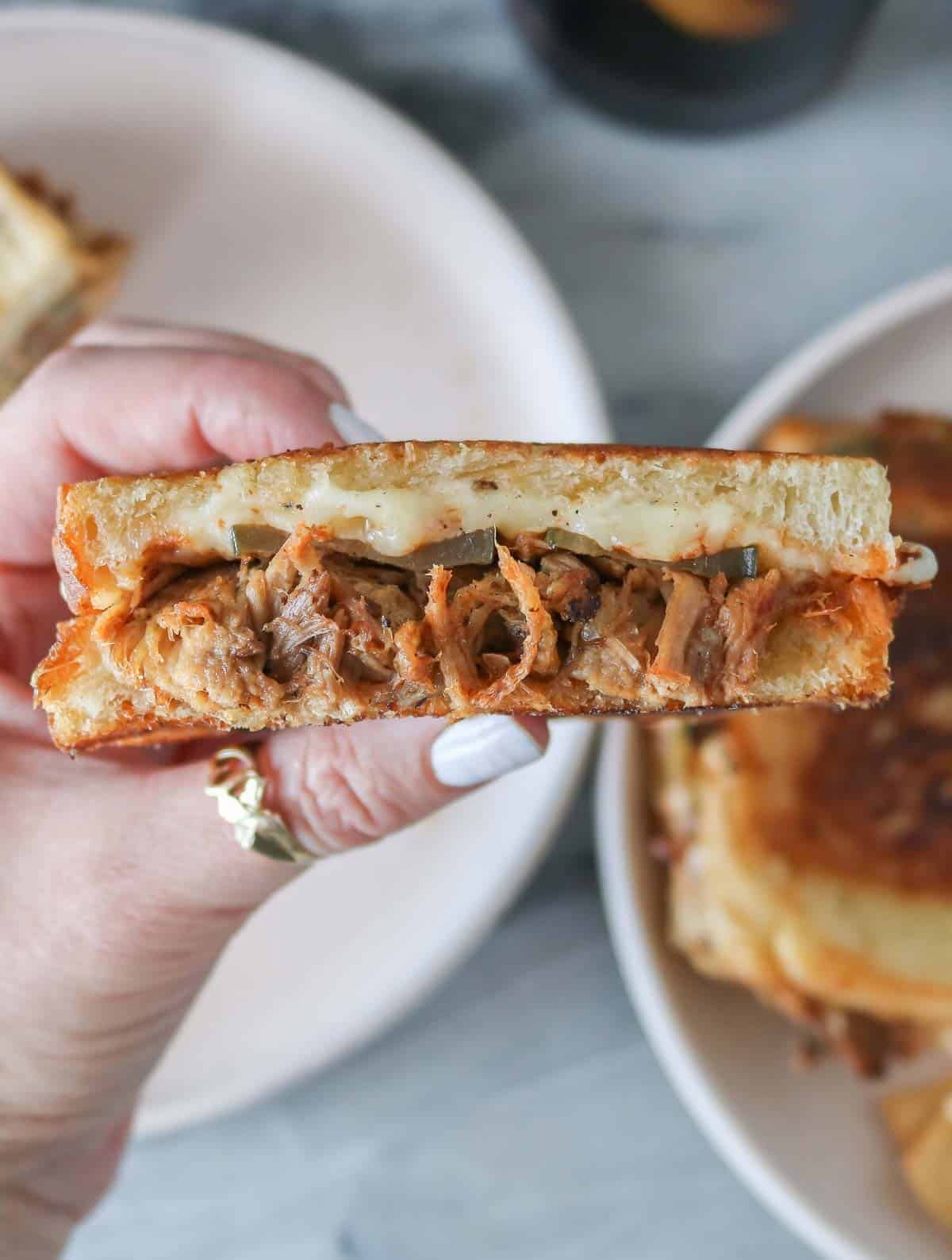 Hand holding one half of a pulled pork grilled cheese sandwich.