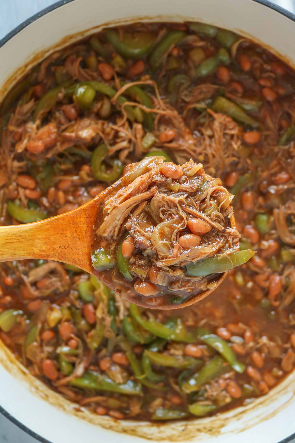 Ladle of pulled pork and beans from a pan.