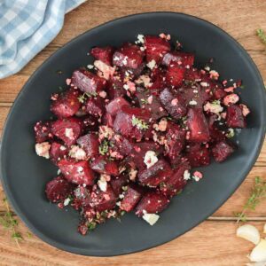 Chunks of roasted beets on a serving platter with crumbled feta and thyme.