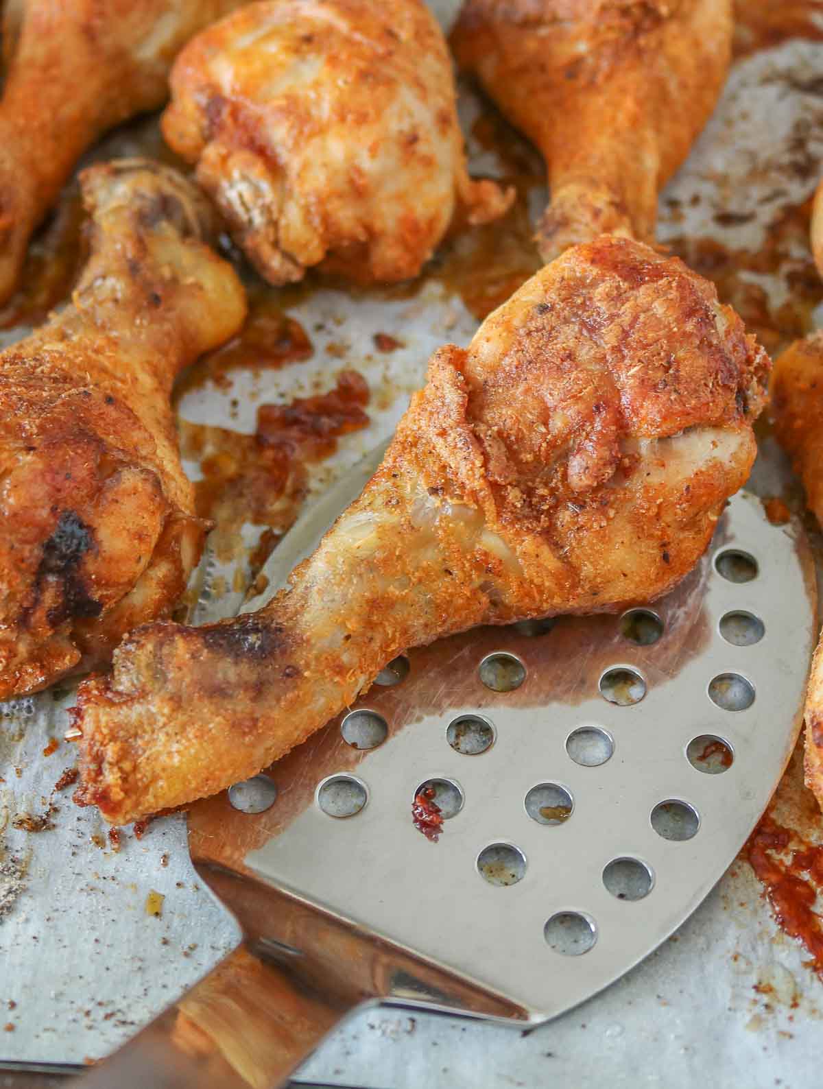 Spatula serving a chicken drumstick from a parchment paper-lined sheet pan.