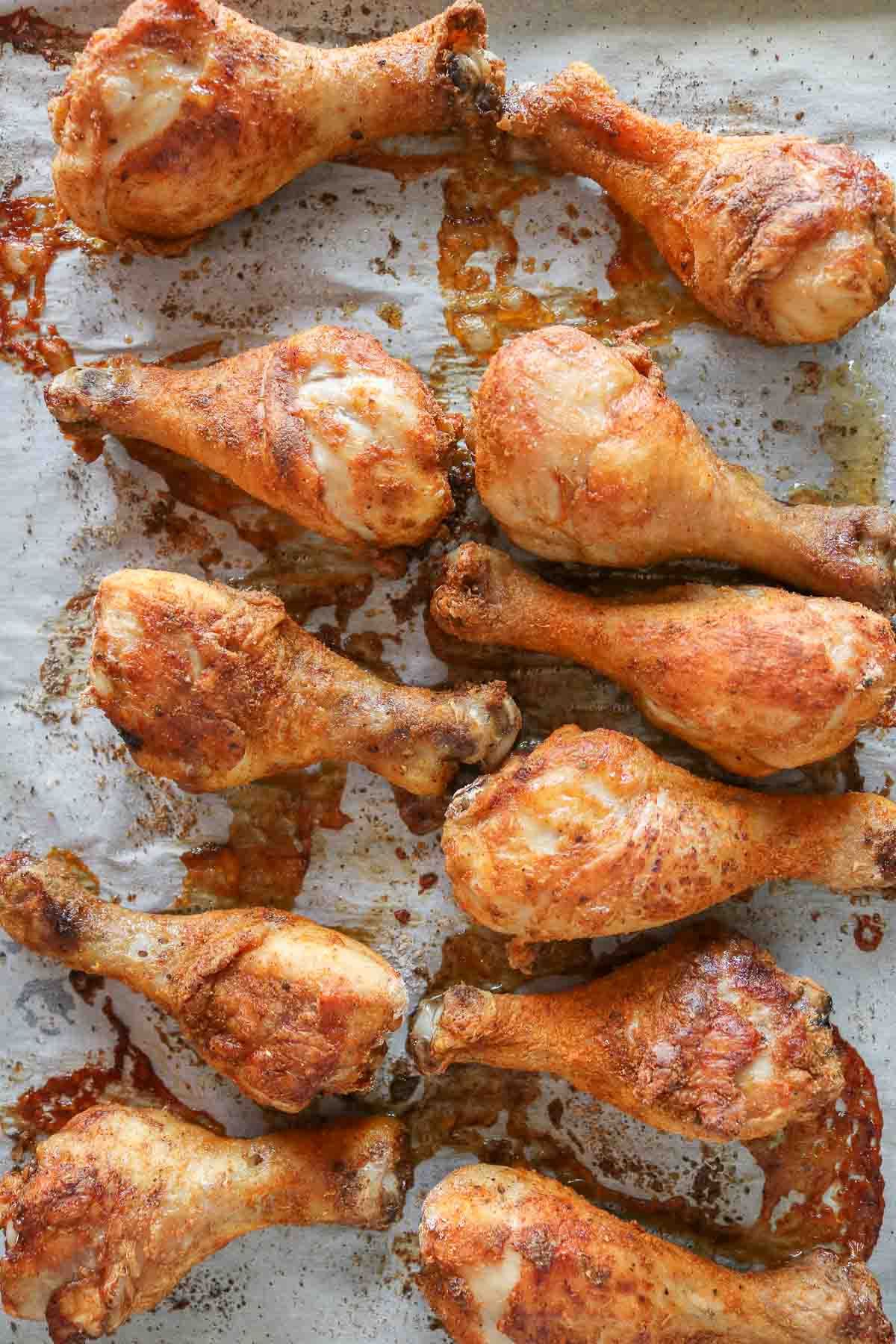 Baked chicken drumsticks on a parchment paper-lined sheet pan.