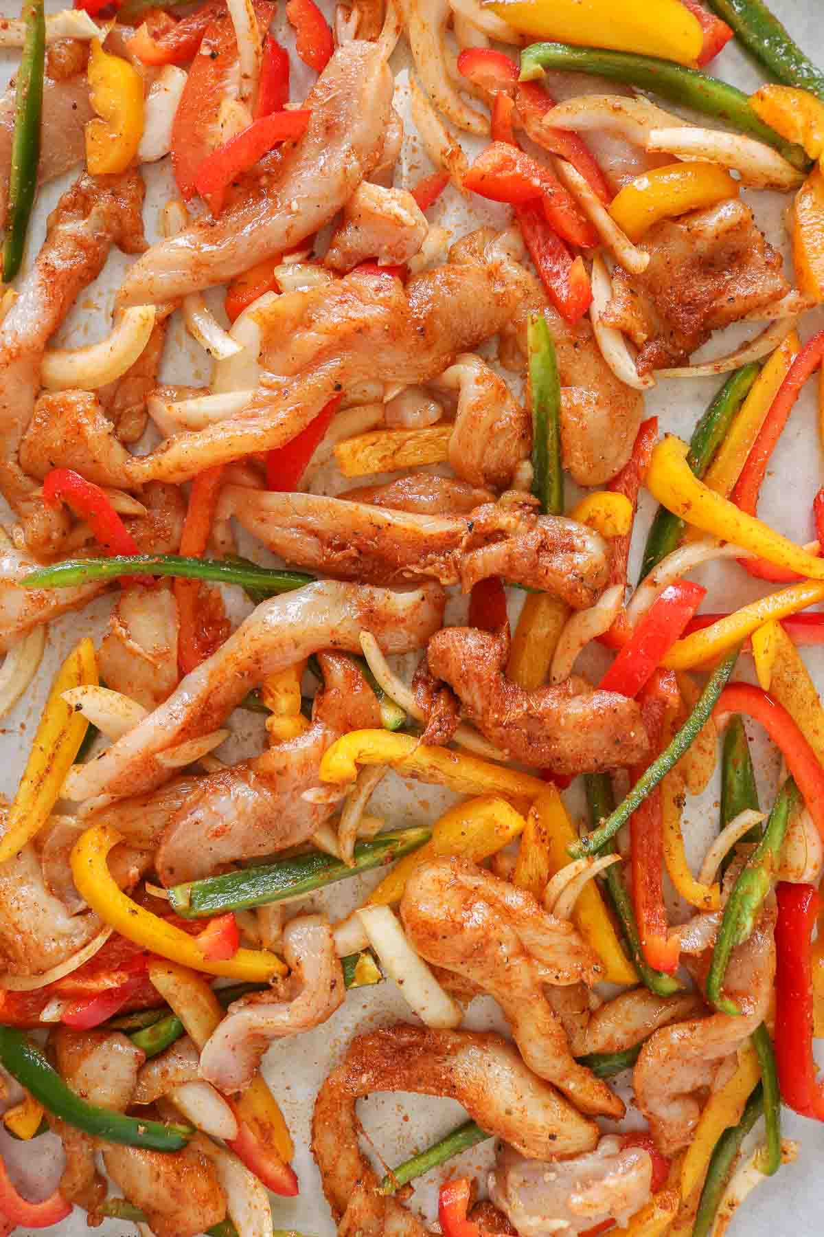 Seasoned chicken, onion and peppers for fajitas on a sheet pan before cooking.