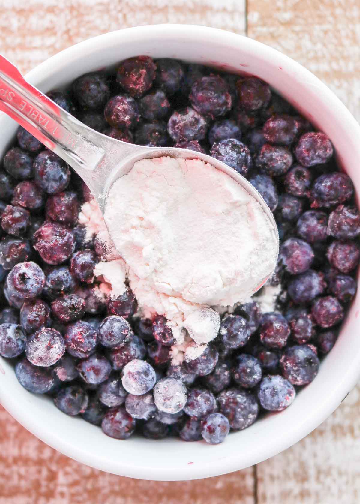 Spoon sprinkling flour over a bowl of blueberries.