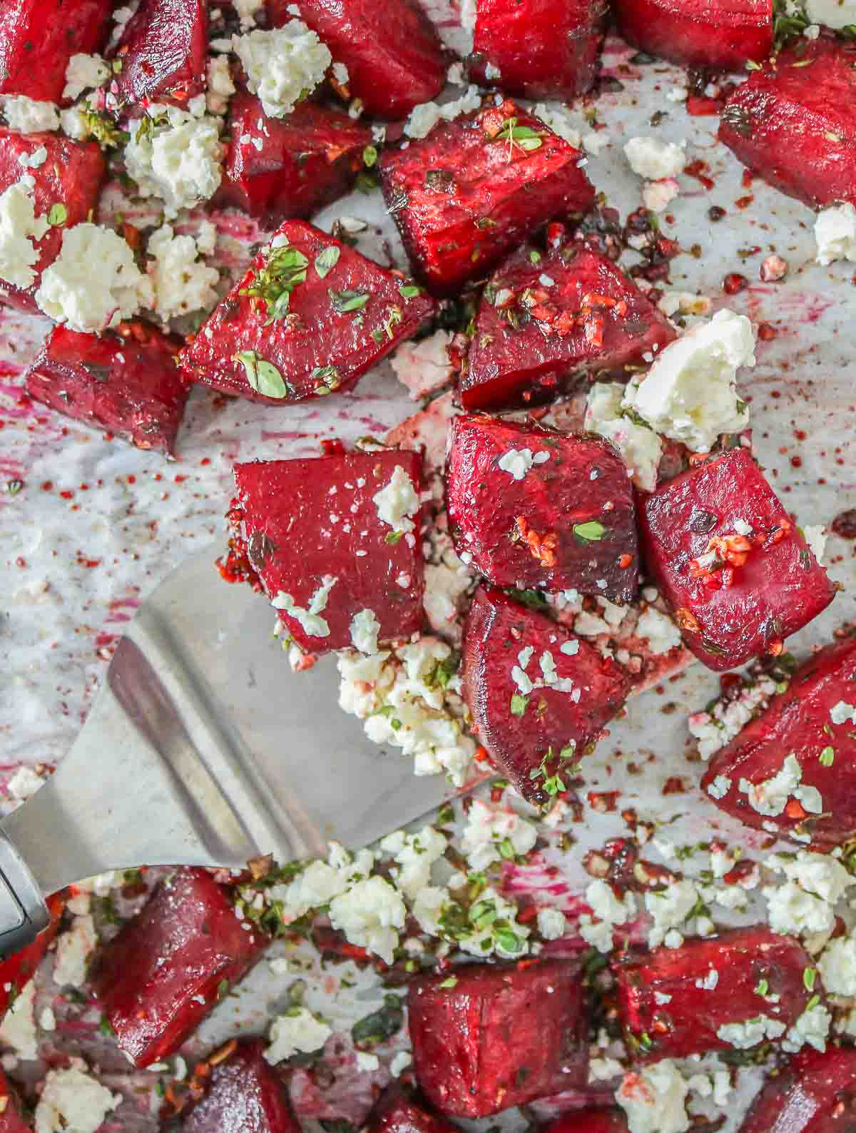 Spatula serving roasted beets with feta from a sheet pan.