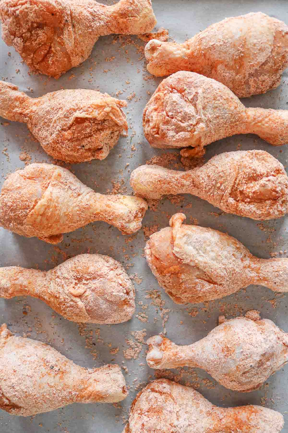 Seasoned chicken drumsticks on a parchment paper-lined sheet pan before cooking.