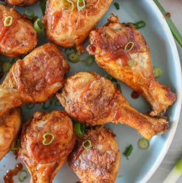 Close-up of baked chicken drumsticks on a blue plate with green onion and barbecue sauce.