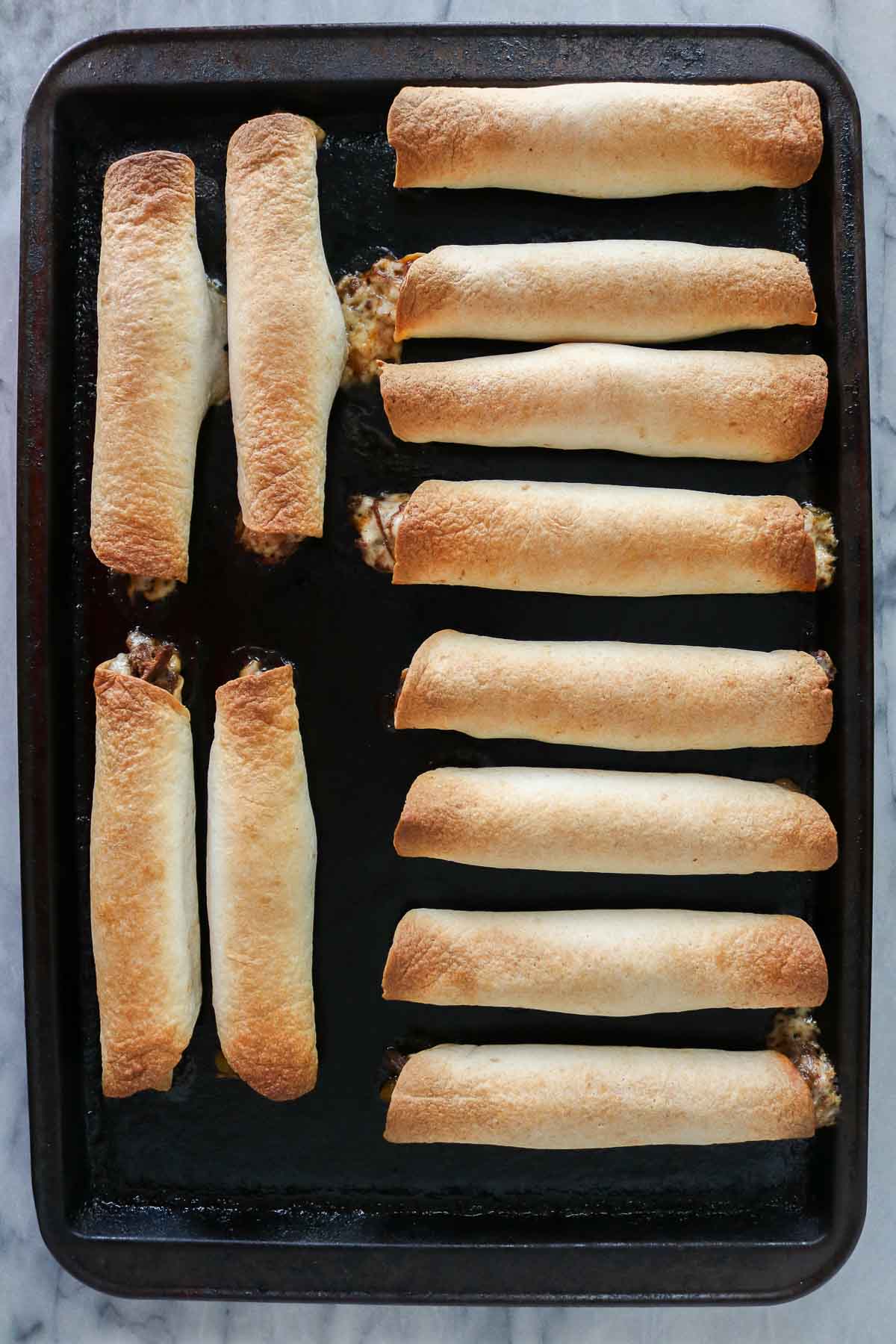 Baked taquitos on a sheet pan.