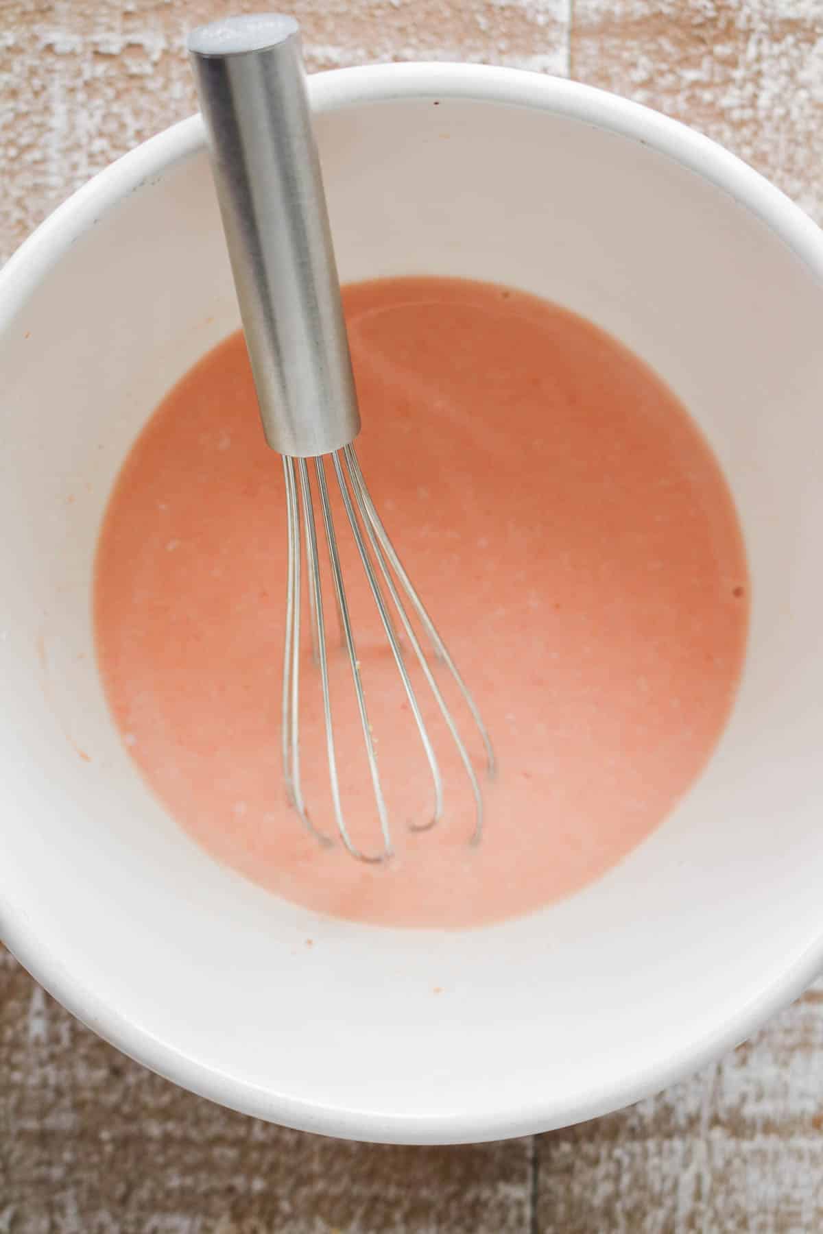 Buttermilk with hot sauce in a bowl with a whisk.