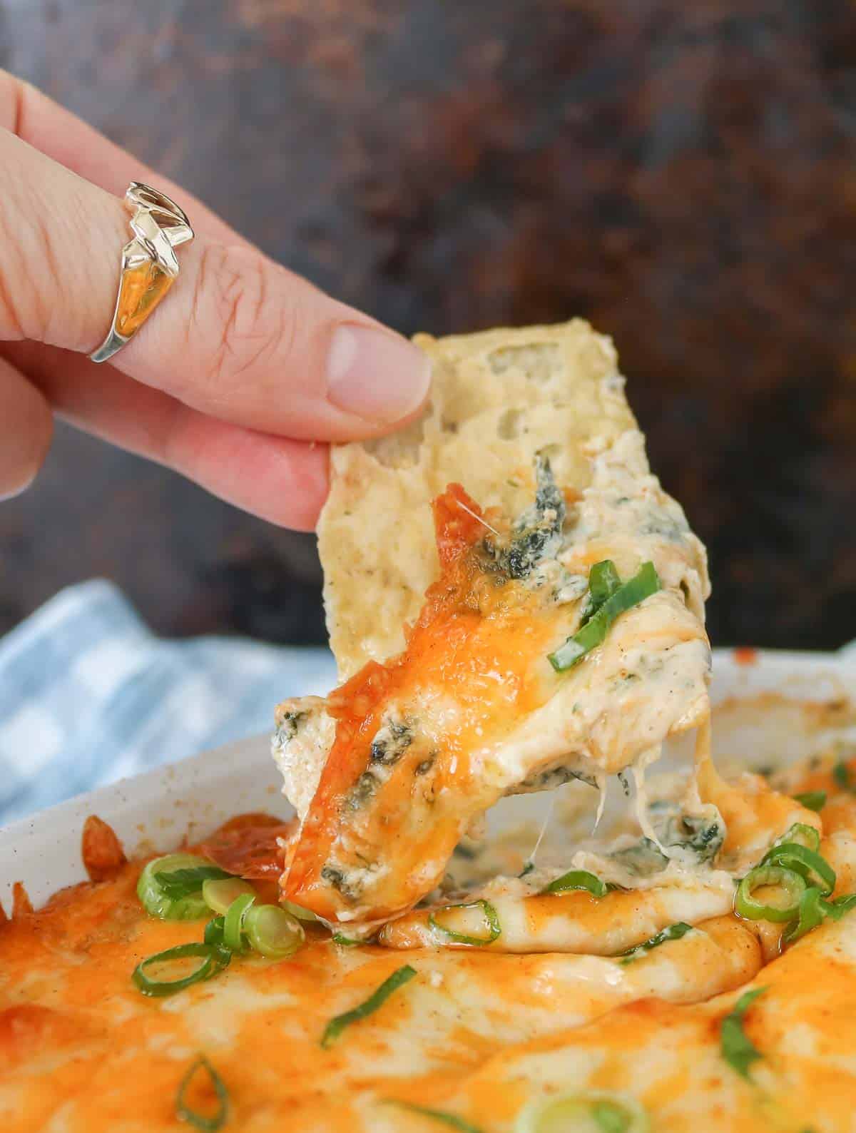 Hand dipping a tortilla chip into cheesy crab dip.
