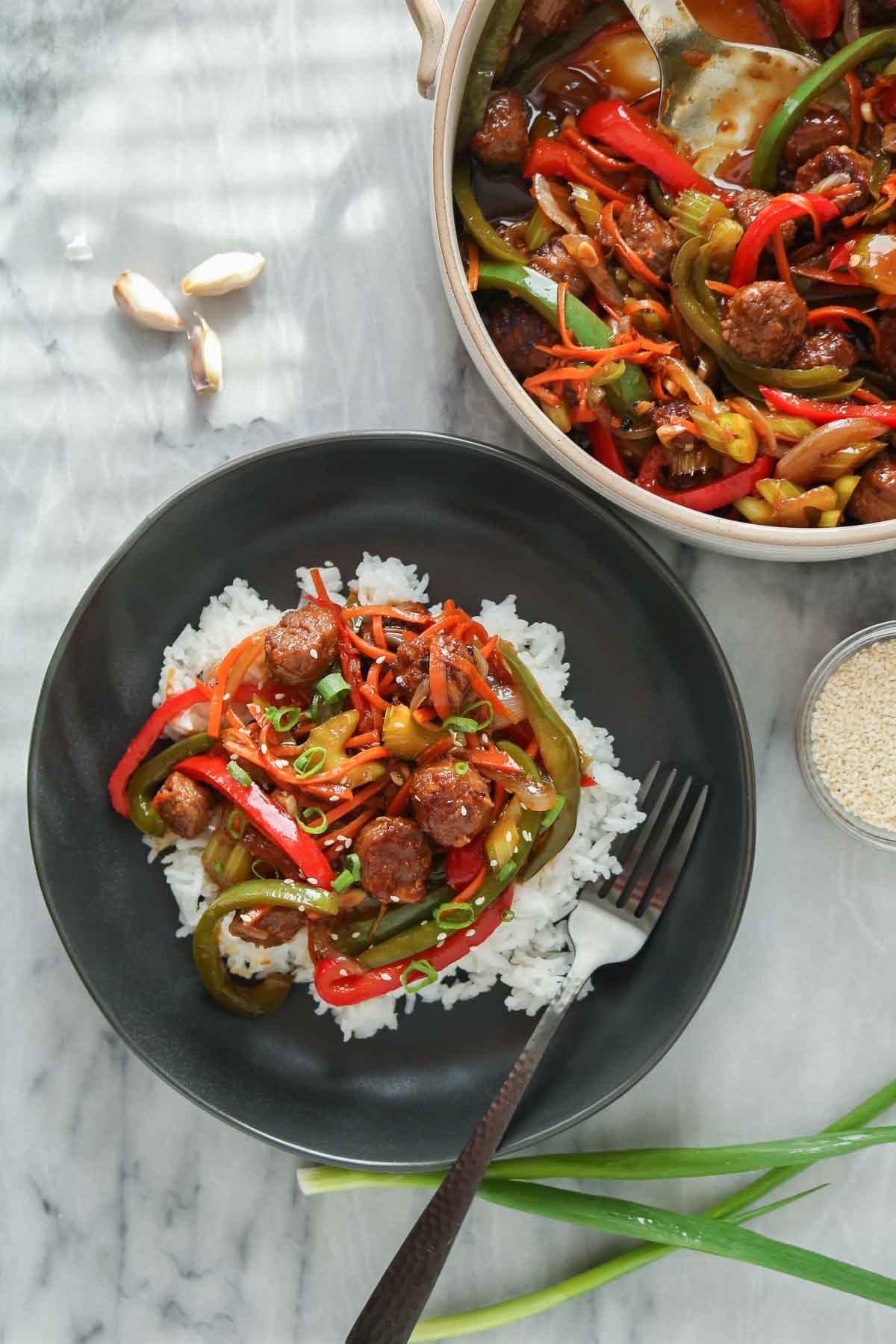 Plate of sausage stir-fry over rice alongside a serving dish of stir-fry.