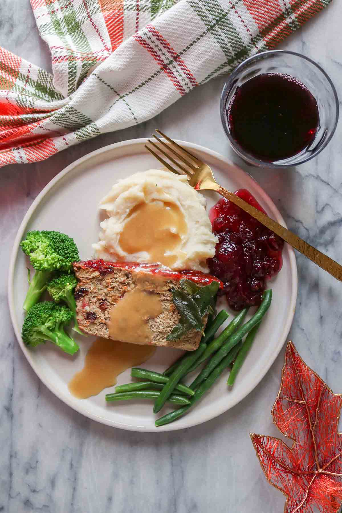 Slice of turkey meatloaf with sides on a plate alongside a glass of red wine.