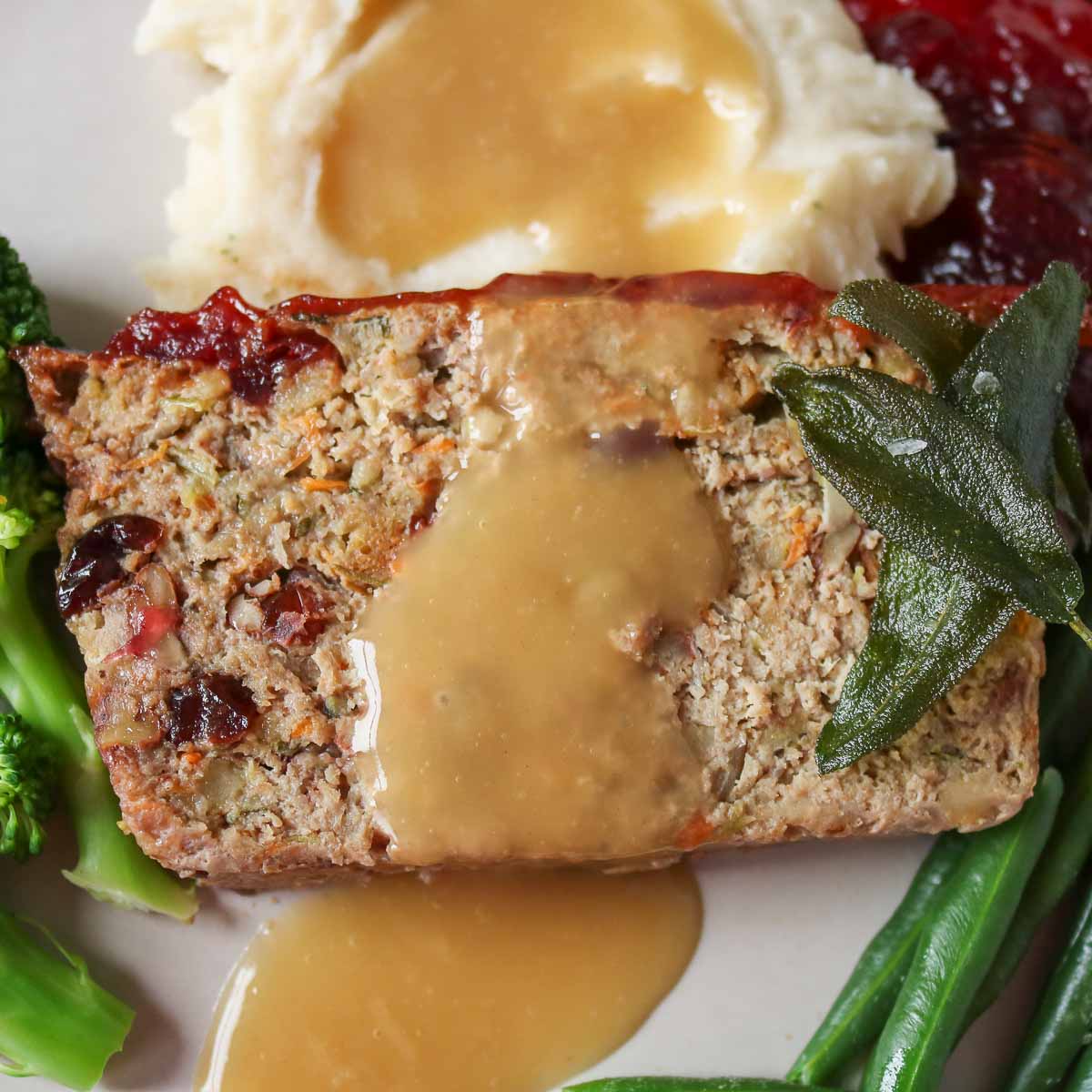 Close-up of a slice of turkey meatloaf on a plate topped with gravy and crispy sage leaves.