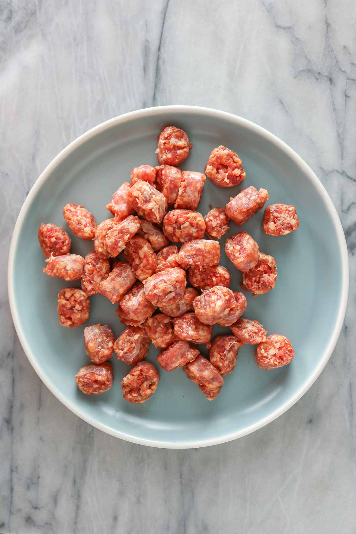 Chunks of uncooked pork sausage on a blue plate.