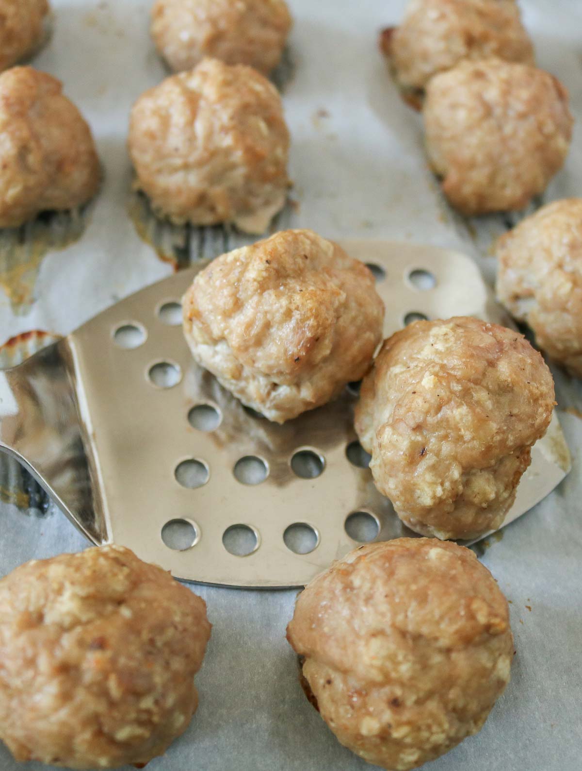 Spatula scooping up baked turkey meatballs from a parchment paper-lined sheet pan.