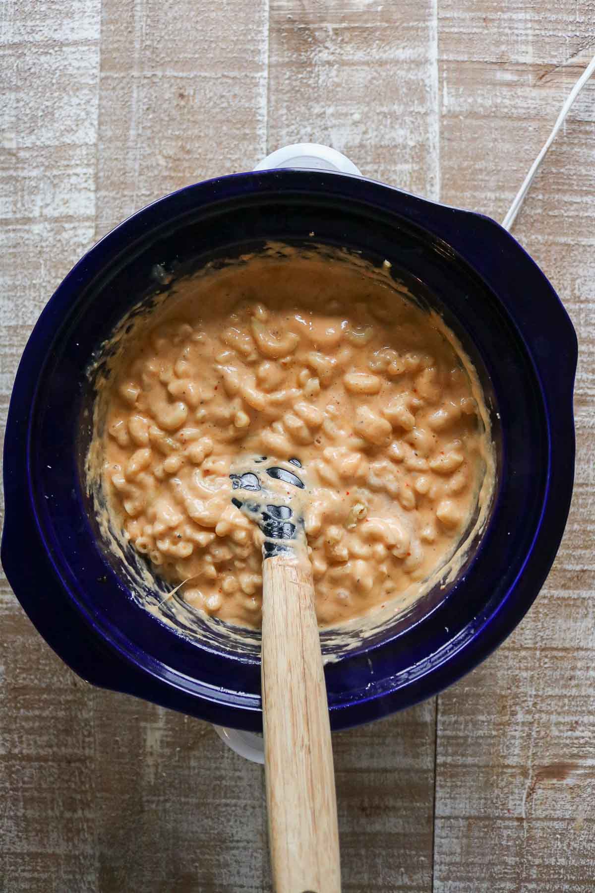 Cheesy mac and cheese in a slow cooker with a spatula.