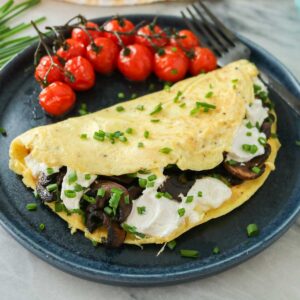 Mushroom and goat cheese omelette on a dark blue plate with roasted tomatoes.