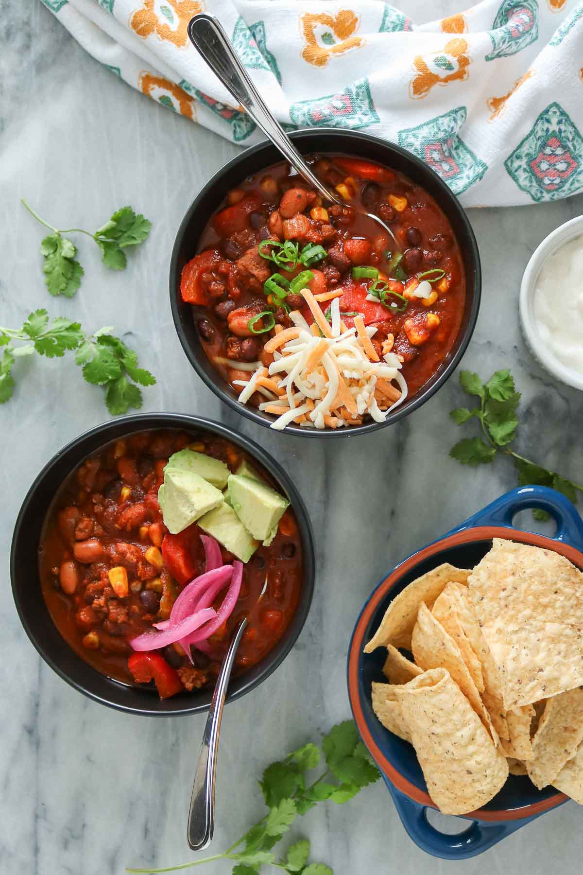 Two bowls of chorizo chili, each garnished with toppings.