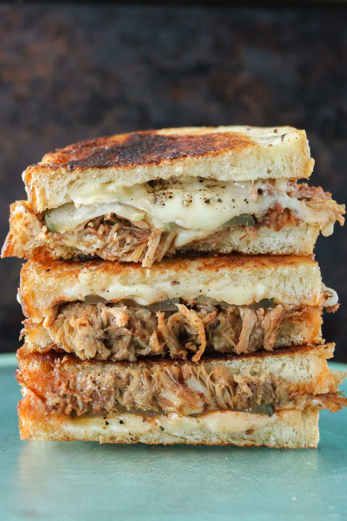 Stack of three pulled pork grilled cheese sandwich halves.
