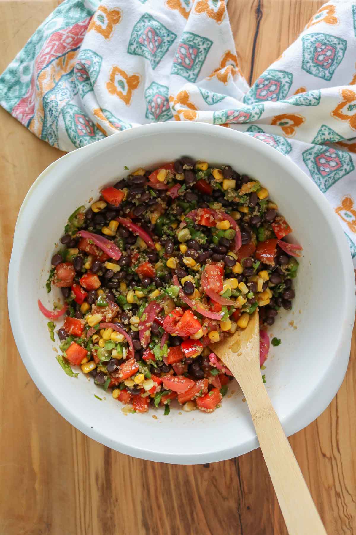 Corn and black bean quinoa salad in a bowl with a wooden spoon.