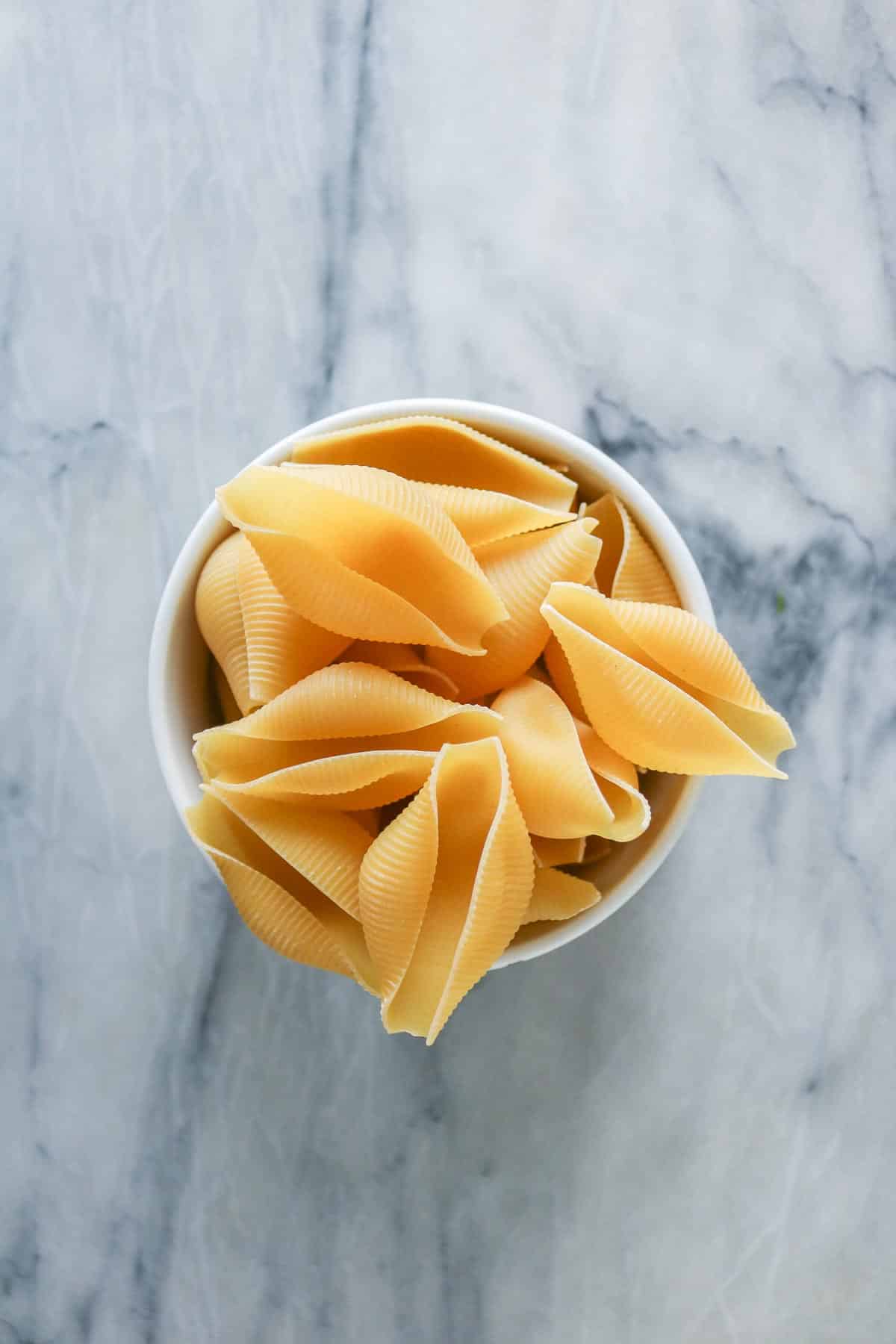 Uncooked jumbo pasta shells in a bowl.