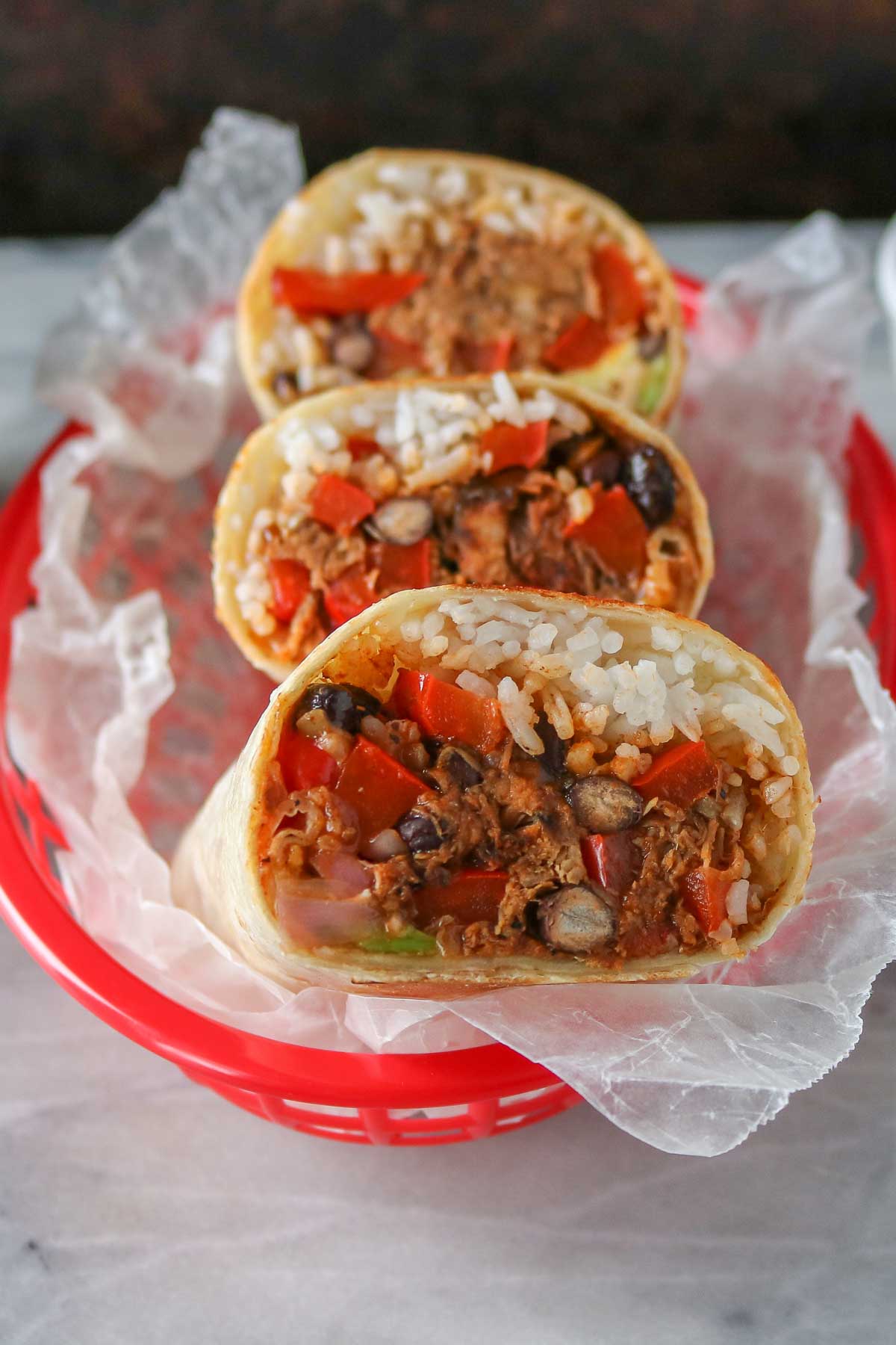 Three pulled pork burritos in a red basket.